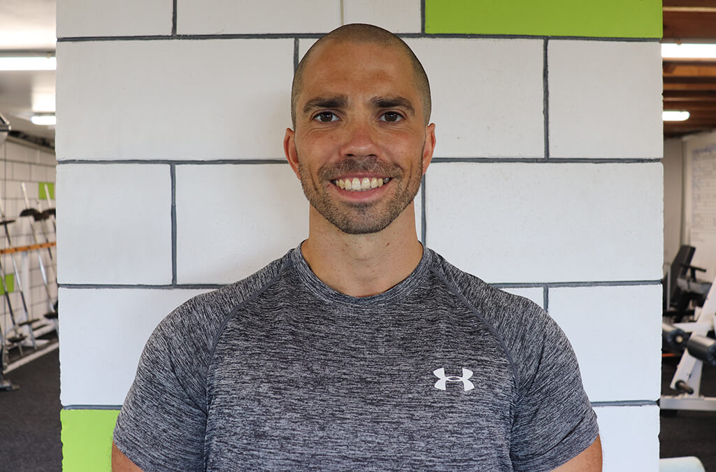 A man in a gray shirt standing in front of a gym.