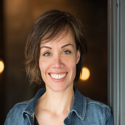 A woman in a denim shirt smiling in front of a door.