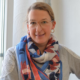 A woman wearing glasses and a scarf in front of a window.