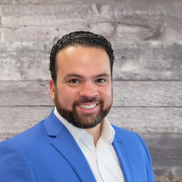 A man in a blue suit smiling in front of a wooden wall.