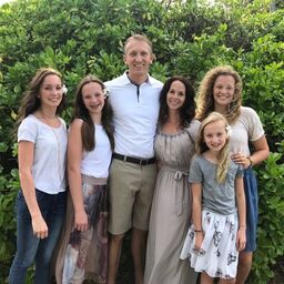 A family posing for a picture in front of bushes.