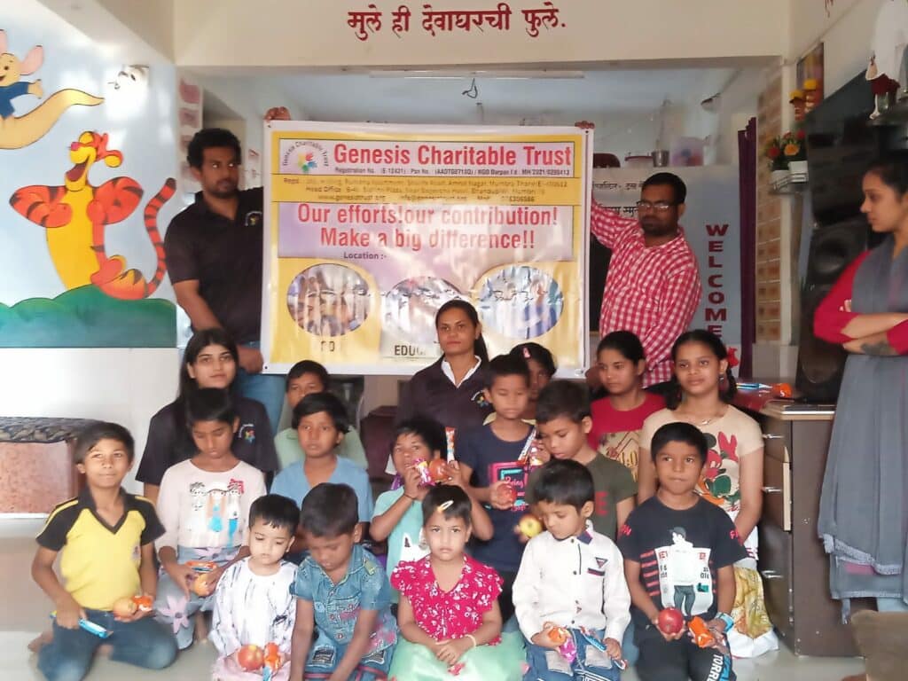 Group of children and adults at a charitable event, holding gifts, standing in front of a banner reading "genesis charitable trust.