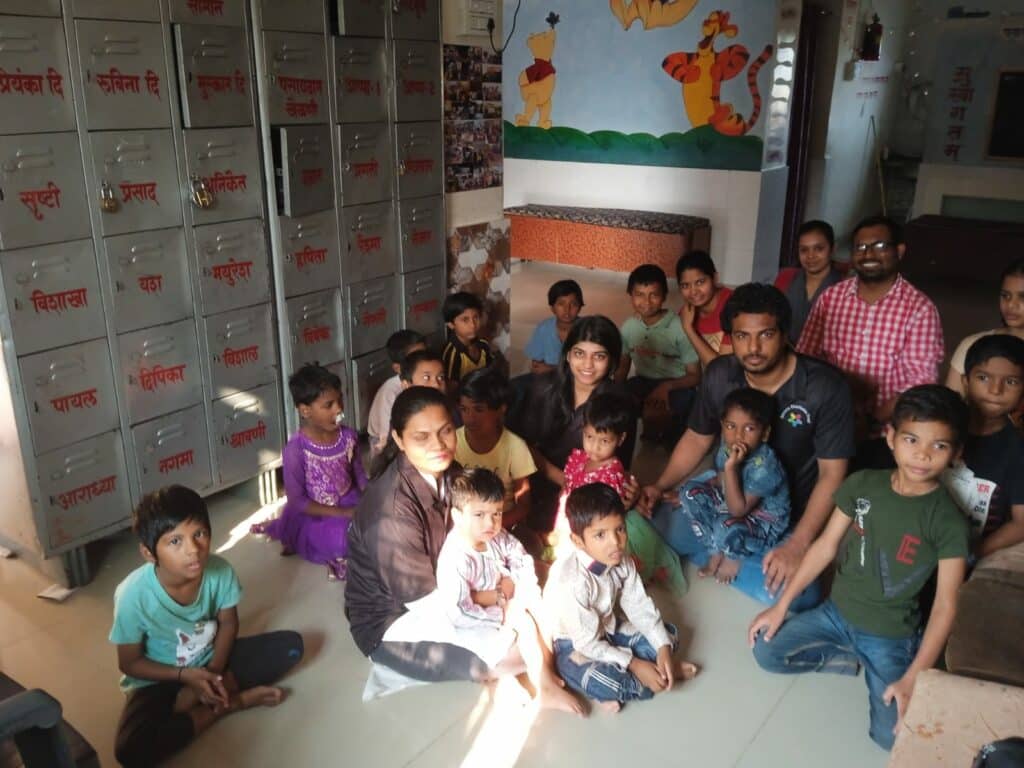 Group of adults and children sitting and standing inside a room with lockers and a decoratively painted wall.