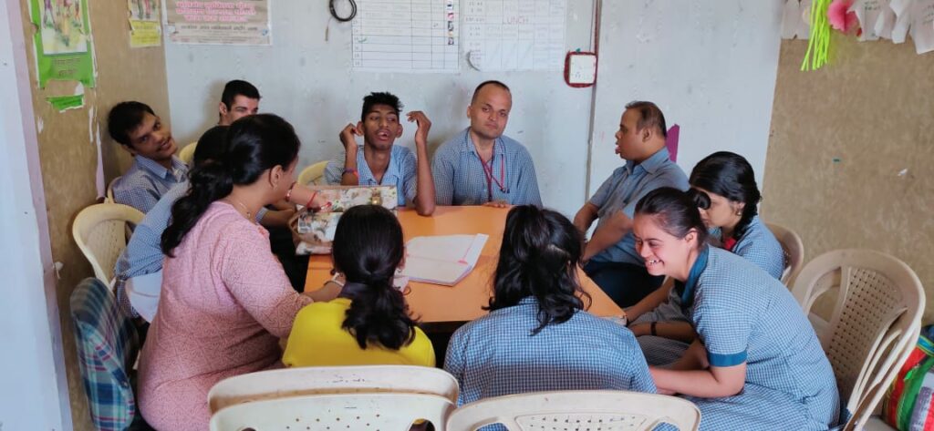 Office staff in uniforms seated around a table having a discussion with documents in a brightly lit room.