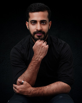 A man in a black shirt posing with his hand on his chin.